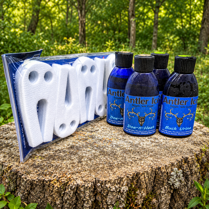 Four blue bottles of Antler Ice doe in heat deer urine attractant and a white foam scent wicks in plastic packaging, displayed on a tree stump with a forest background.