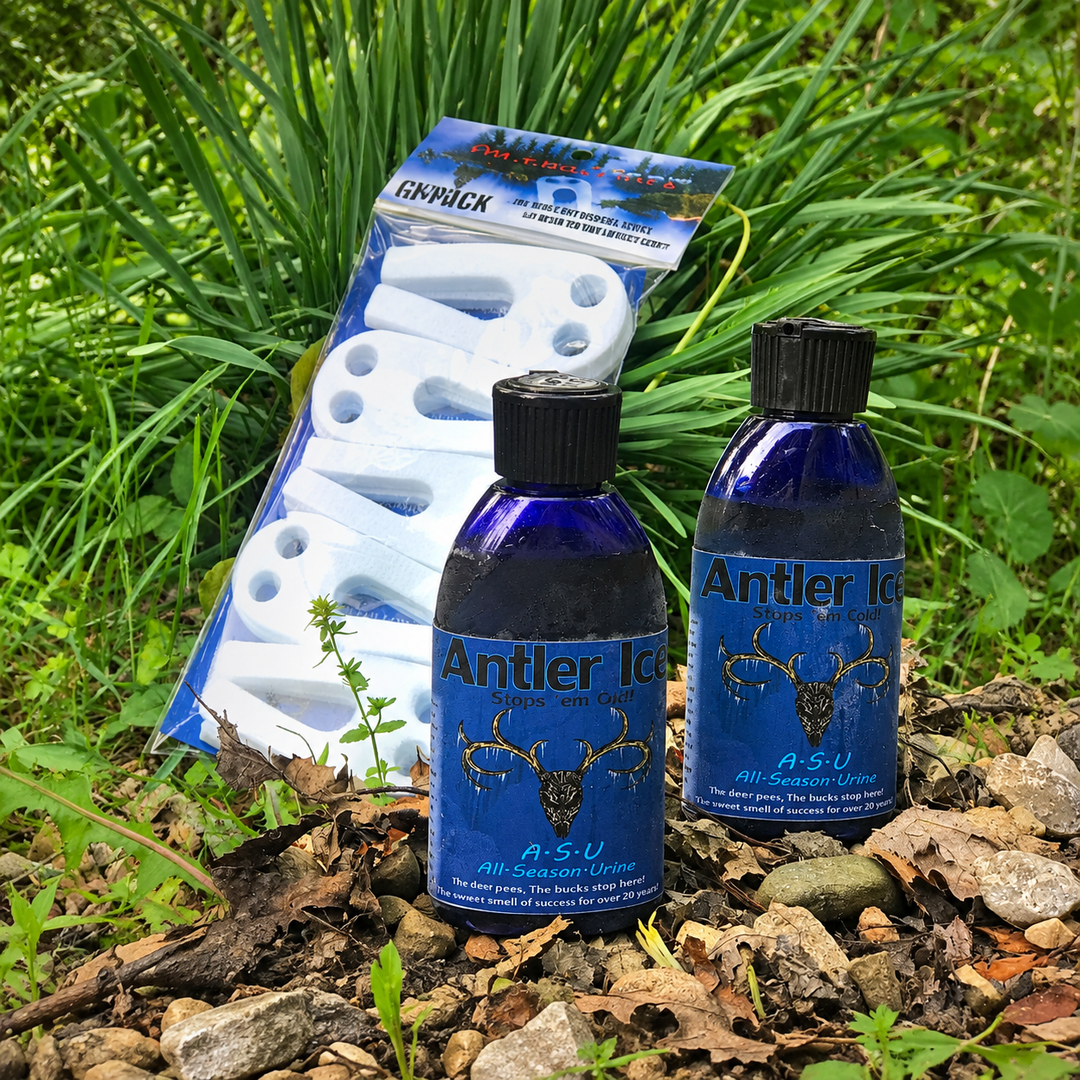 Two blue bottles of Antler Ice A-S-U All-Season Ice and a package of white absorbent scent wicks placed outdoors on rocks and grass.