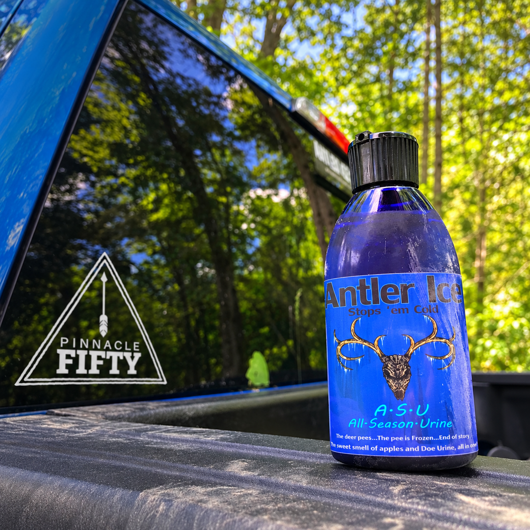A bottle of Antler Ice Stops 'Em Cold A-S-U All Season Urine placed on the tailgate of a blue pickup truck with a forest background.