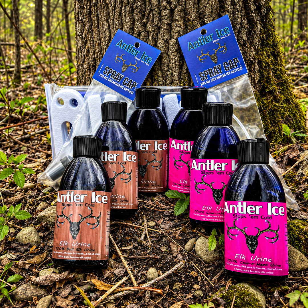 Six bottles of Antler Ice elk urine and scent wicks arranged on the forest floor in front of a tree trunk, with two blue spray cap tags and a clear plastic bag visible behind them.