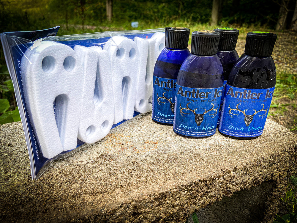 A product image featuring a pack of white foam ghost wicks and three blue bottles, two labeled Antler Ice Doe-n-Heat and one labeled Antler Ice Buck Urine on a concrete block surface.